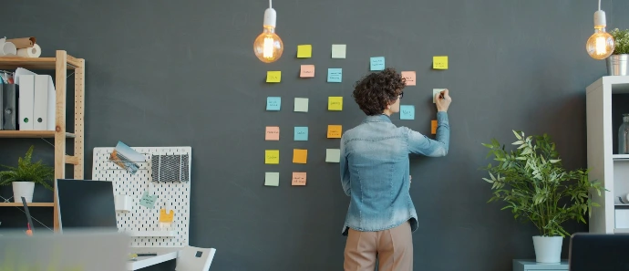Woman writing on sticky notes on a wall.
